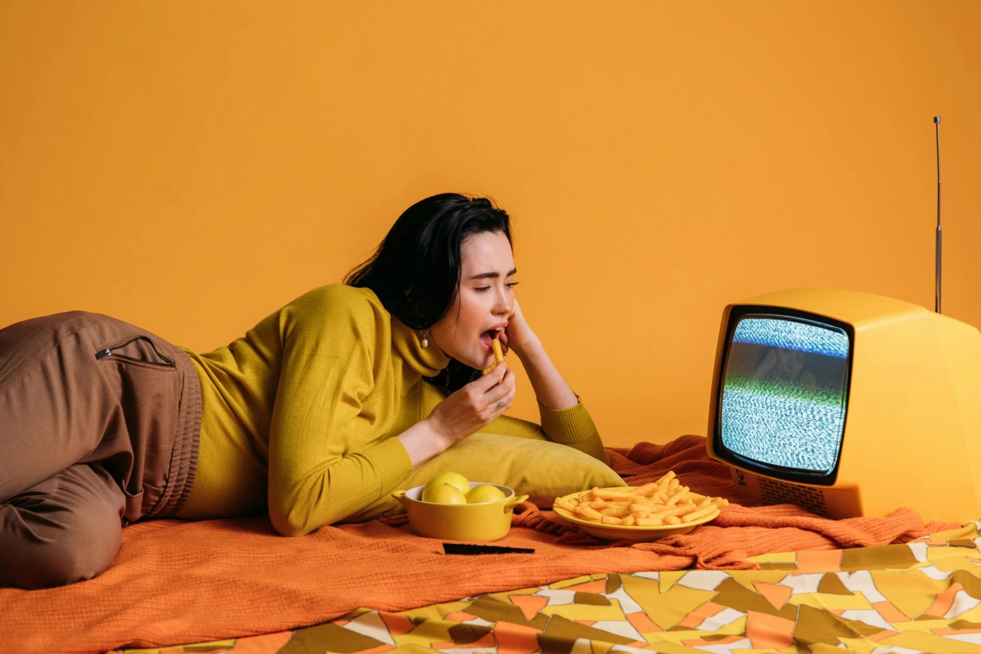 Jeune femme allongée devant un téléviseur vintage sur fond ocre