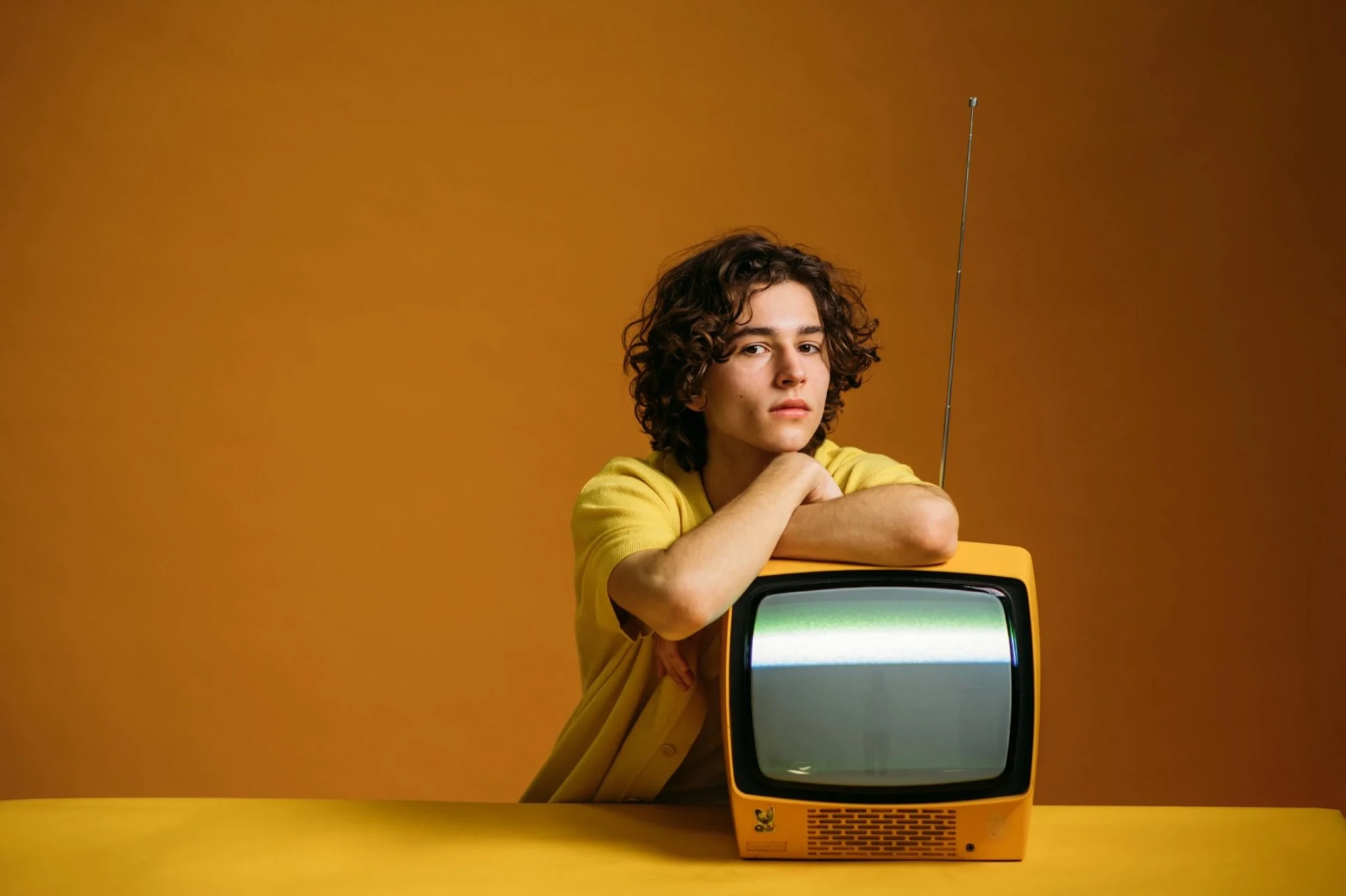 Jeune homme accoudé à un téléviseur vintage sur fond ocre