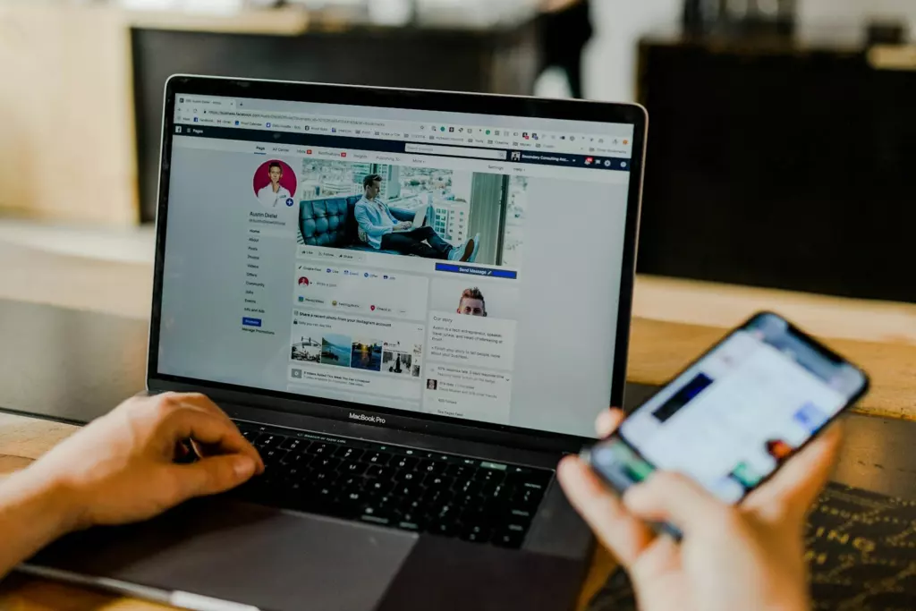 Une Page Facebook ouverte sur un ordinateur portable, un smartphone à la main
