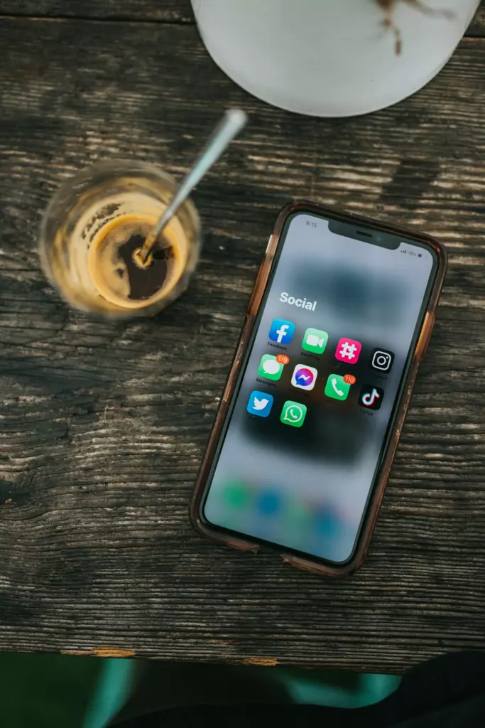 Smartphone affichant des applications de réseaux sociaux, posé sur une table en bois à côté d'un café